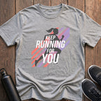 Gray t-shirt with running-themed design on a wooden surface with sneakers and a water bottle.